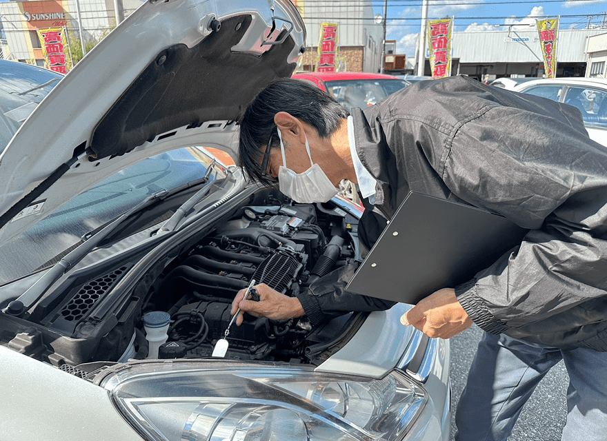 ボンネットを開けてエンジン内部を確認する整備士