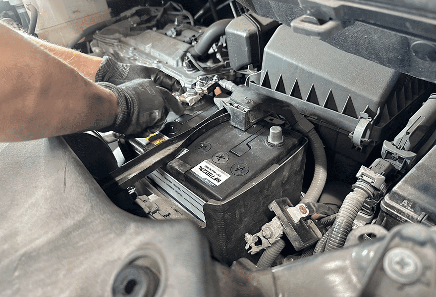 車のエンジンルーム内でバッテリーのメンテナンスをする整備士