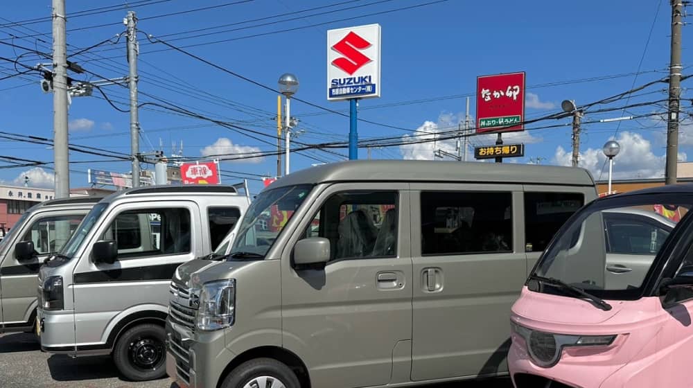 スズキの販売店の駐車場に並ぶ軽自動車とピンクの電動三輪車