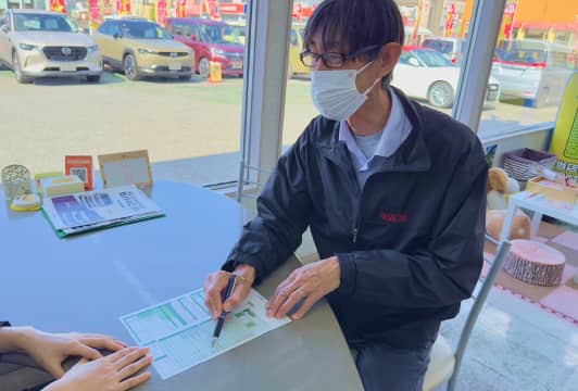 自動車販売店で契約書に署名するお客様とスタッフ