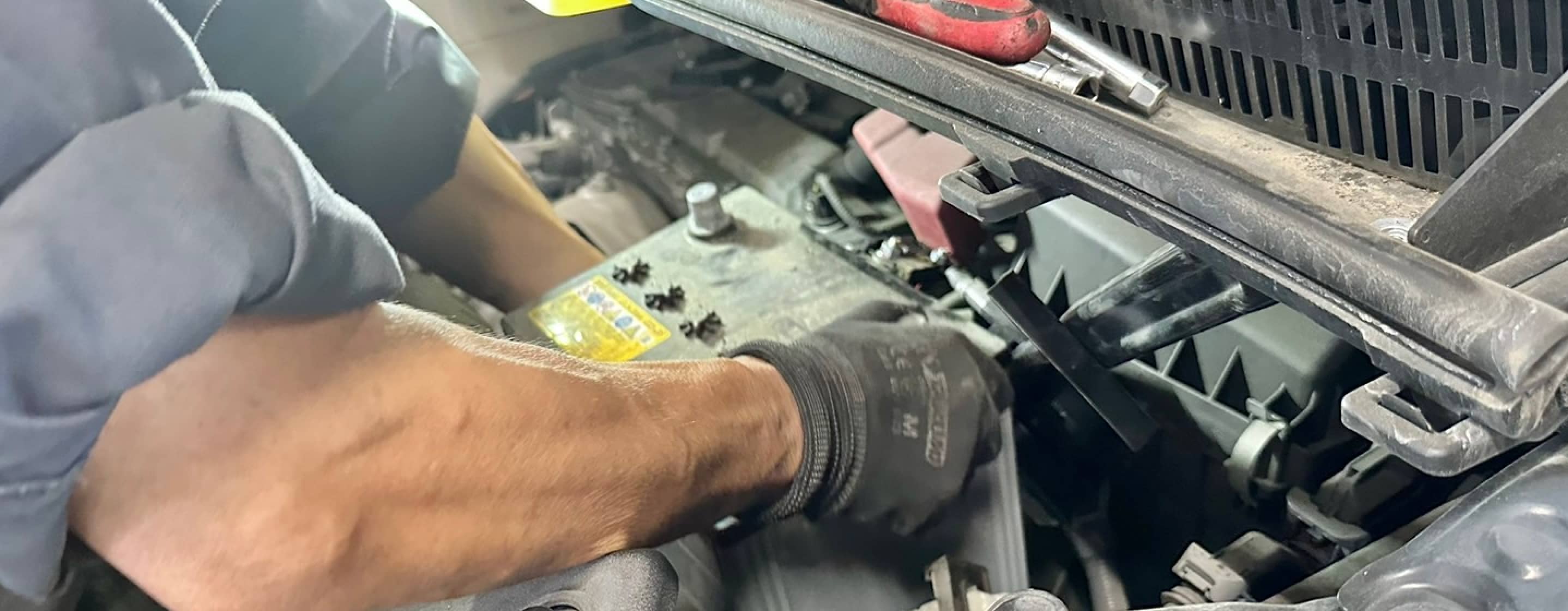 整備士がエンジンルーム内でバッテリー交換作業をしている様子