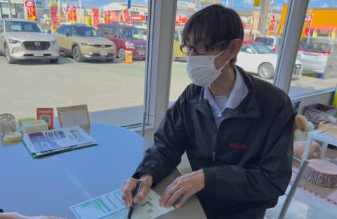 自動車販売店で書類に記入するマスク姿の男性スタッフ